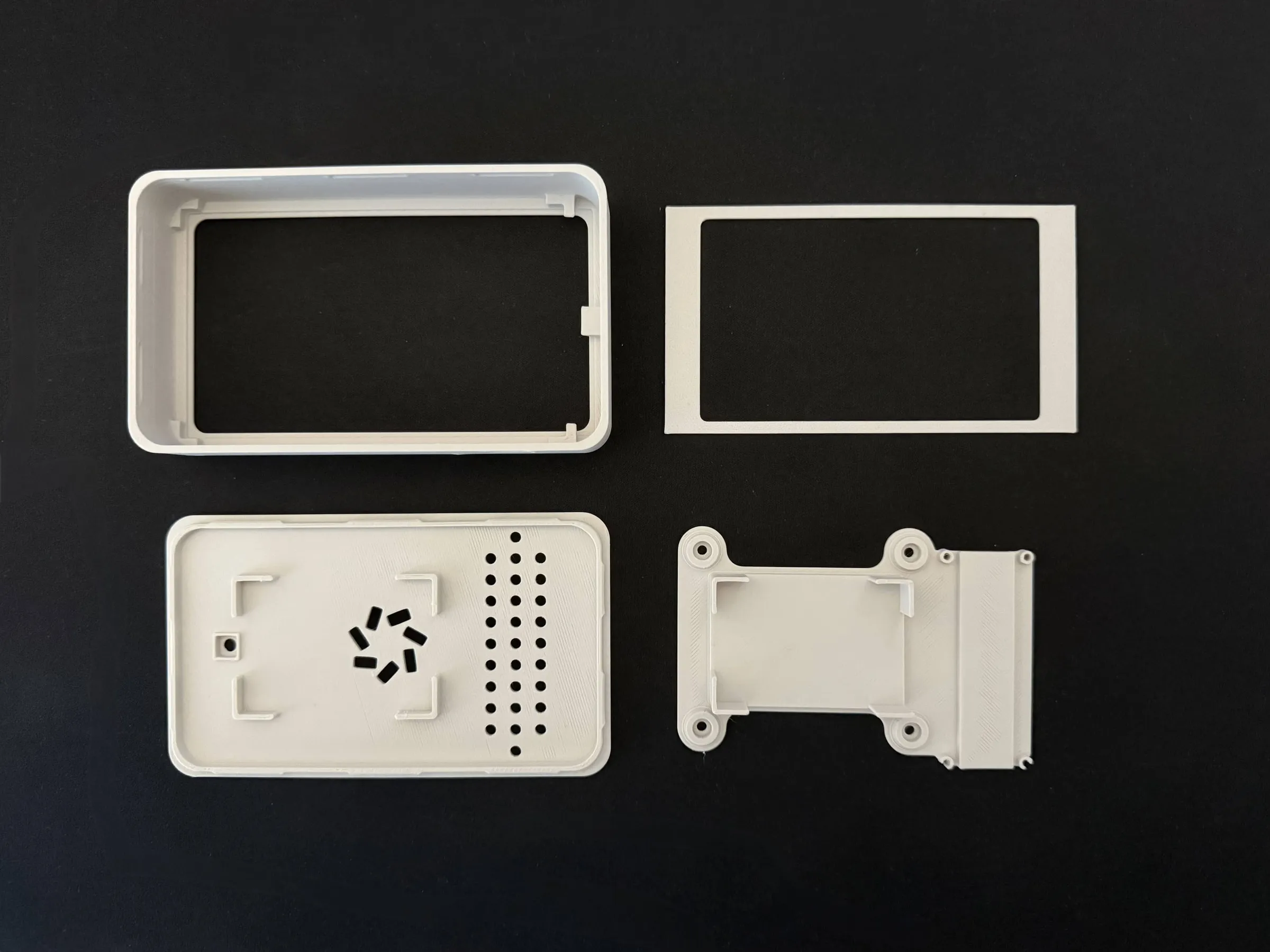 The four printed case parts laid out on black: the front frame, the thin display ring, the back with vent holes and the midframe