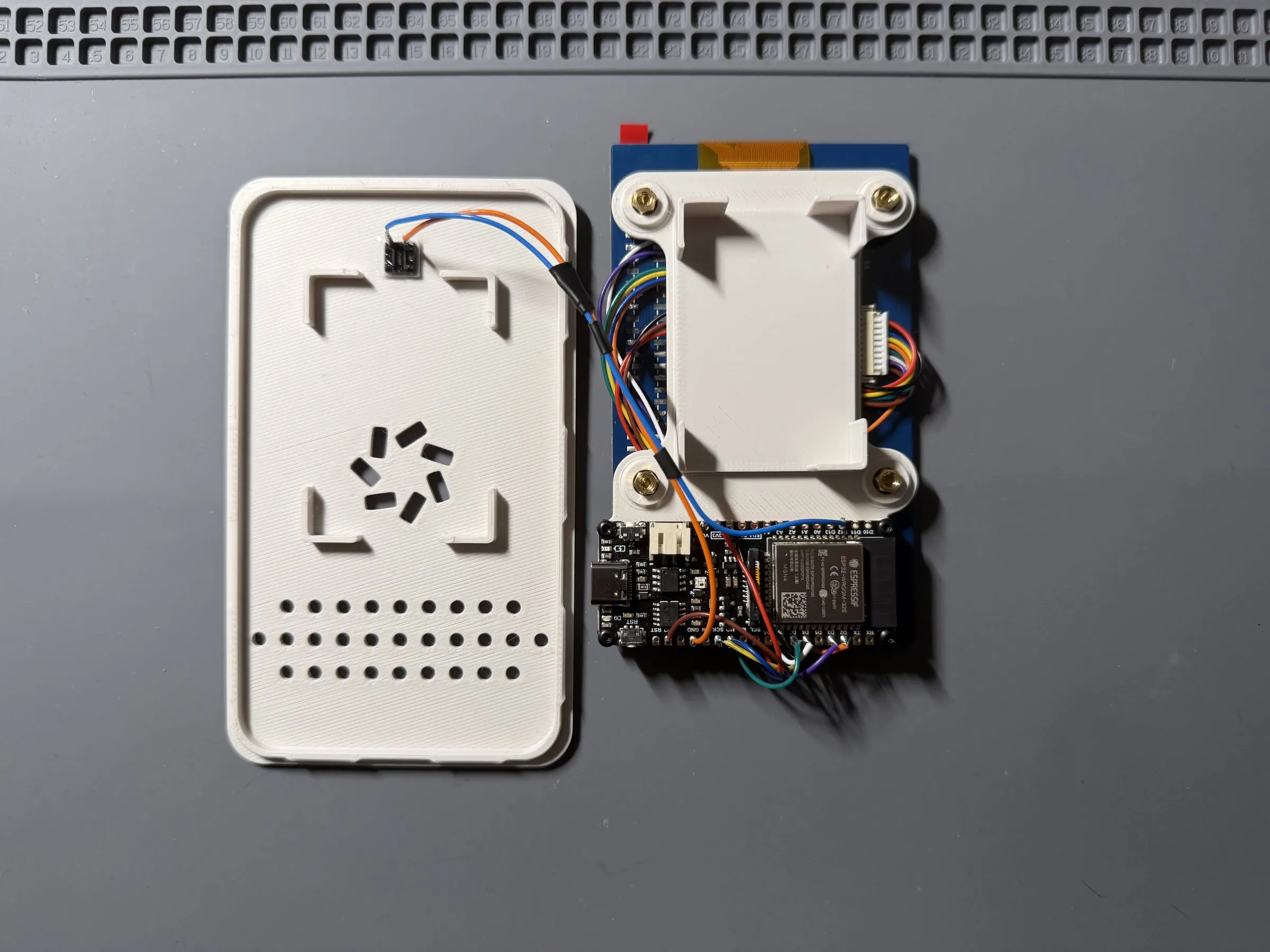 The mini opened up: the back panel with the button wired to it, and next to it the back of the display with the midframe screwed on, the dev board below it and coloured wires between them
