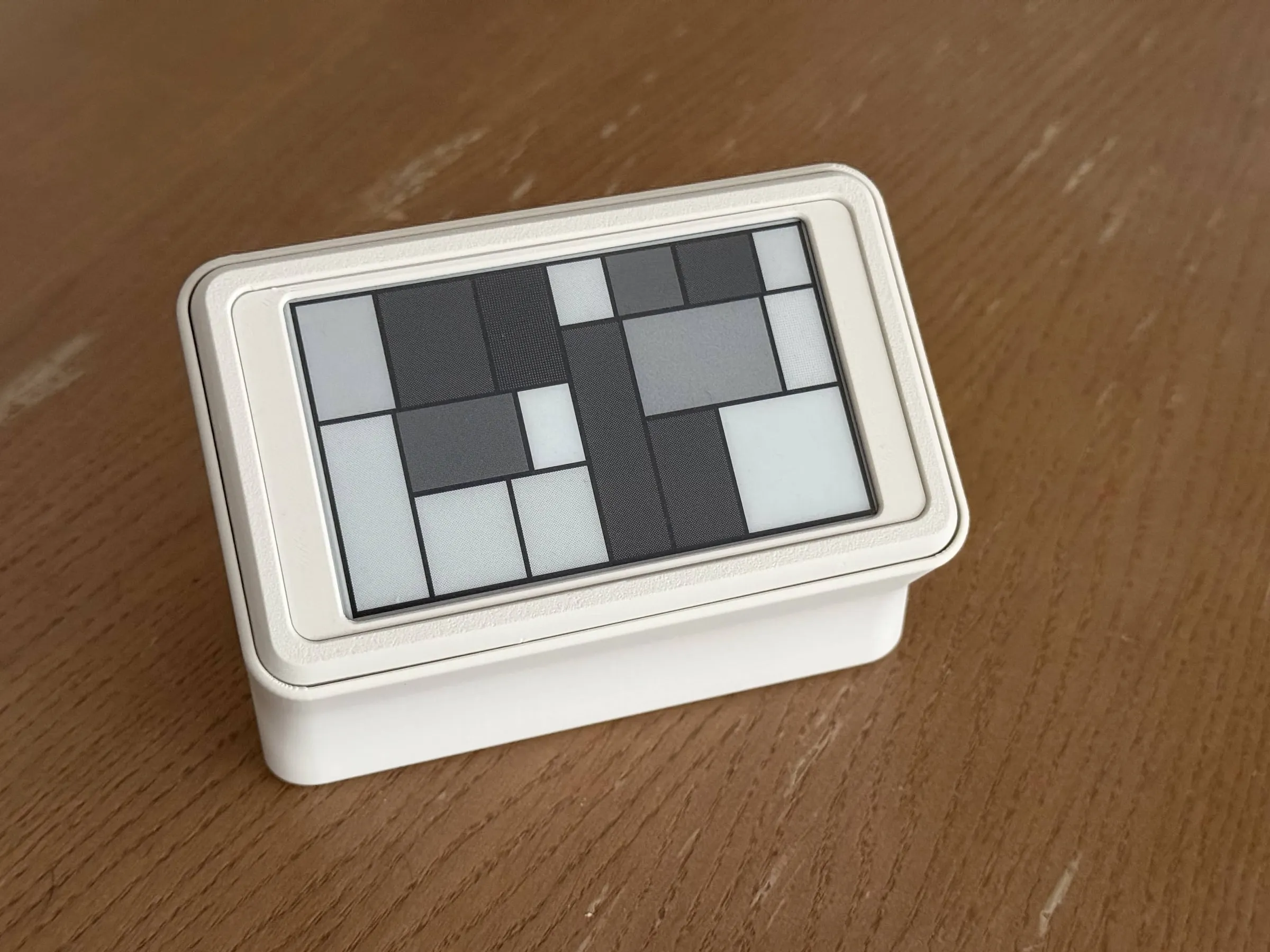 The mini in its stand on a wooden table, tilted back at a low angle, the screen showing a pattern of grey rectangles